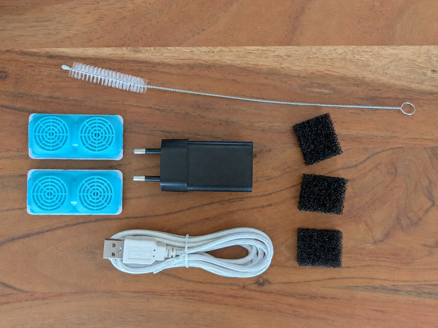 Zubehörübersicht mit Filtereinsätzen, schwarzen Schaumstoffstücken, Netzteil, USB-Kabel und Reinigungsbürste.